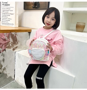 Girl wearing a sequin heart backpack with cute wings, sitting in a studio setting