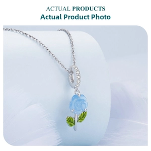 Macro detail of a light blue rose pendant with green leaves and zircon-set bail