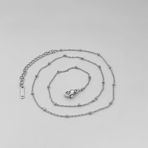 Detailed close-up of a silver stainless steel bead necklace featuring a lobster clasp and chain