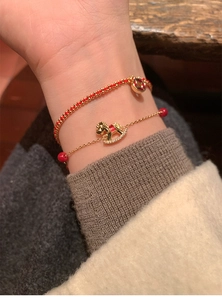Detailed close-up of 18k gold plated horse bracelet with red enamel and zircon stones