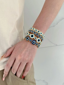 Detailed view of stacked gold evil eye bracelets with blue enamel on model's wrist