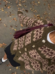 Close-up of vintage jacquard knit cardigan with ornate metal buttons on leaf background