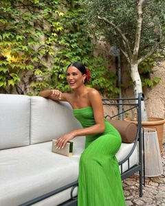 Close-up of green strapless pleated midi dress with gold clutch bag in garden setting