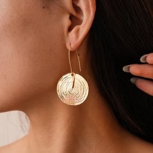 Close-up of golden geometric earrings with spiral texture on a model wearing them