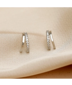 Macro shot of silver S925 earrings with double curved zircon rows on silk fabric