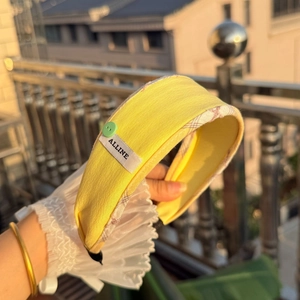 Detail of yellow fabric headband with green button and stitched ALLINE brand label