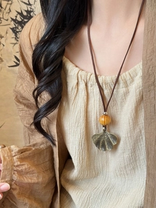 Detail of bronze ginkgo leaf pendant with wooden bead on brown leather cord