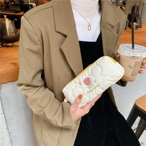 Detail of white quilted pouch with tulip embroidery and yellow zipper in a lifestyle setting