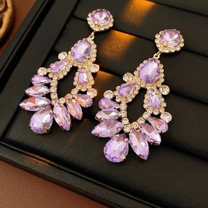 Macro shot of gold tassel earrings with purple water drop crystals on black display