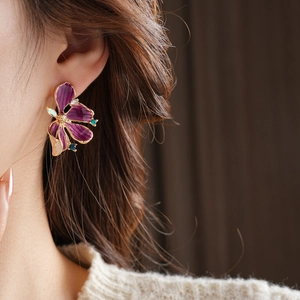 Nahaufnahme von Vintage-Blumenohrringen mit lila Emaille und Goldrand am Modellohr