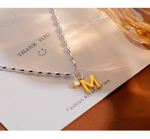Detailed shot of golden letter M pendant with zircon on a silver bead chain jewelry