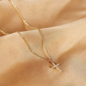 Detailed view of an 18K gold plated cross pendant with CZ stones on champagne silk
