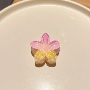 Detailed macro view of a pink and yellow gradient frangipani hair claw with glitter