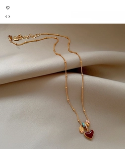 Detail of 18k gold plated heart necklace with colorful enamel charms on silk fabric