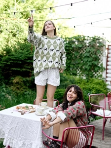 Outdoor shot of two women wearing cherry print and diamond pattern knit sweaters