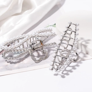 Detailed close-up of large pearl metal hair claws in silver on white silk background