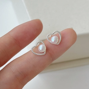 Detailed close-up of hollow heart pearl stud earrings worn on finger for size scale
