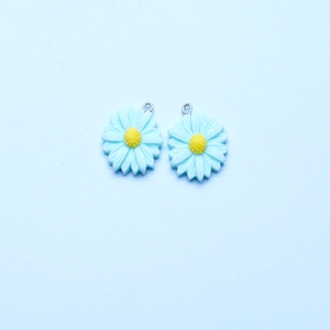 Detail shot of light blue daisy flower resin charms with yellow centers and silver rings