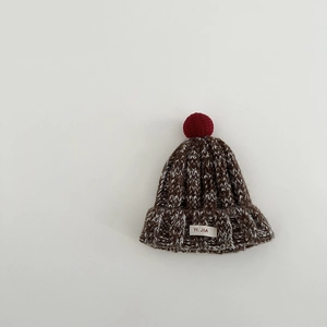 Detail der grob gestrickten braun-weißen Textur mit rotem Bommel und gewebtem Etikett
