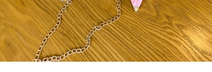Detail of a gold chain strap with pink charm accent on a natural wood surface