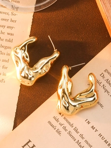 Detailed shot of golden irregular liquid-style hoop earrings on vintage newspaper background