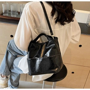 Close-up of black glossy pleated tote bag with adjustable strap worn on the shoulder