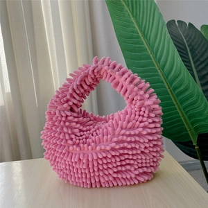 Detailed side view of pink fluffy plush handbag on wooden table with green leaves