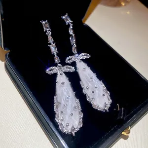Elegant silver bow and teardrop earrings with sparkling zircons on black velvet display