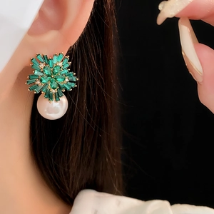 Detail of gold flower earring with green crystals and a white pearl on a model