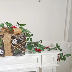 Detail of Christmas rattan gift box with golden bow, holly leaves, and red berries decor