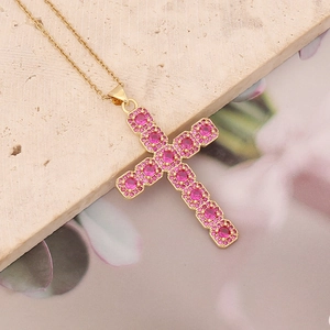 Close-up of gold cross necklace featuring pink round-cut cubic zirconia on a stone tile