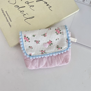 Quilted floral pouch with pink heart button and blue pom-pom trim on vintage books