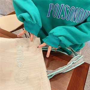 Detail of embroidered smile on beige canvas tote with braided colorful tassel strap