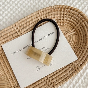 Detail of a brown acetate geometric hair tie with handmade gold lettering on white card