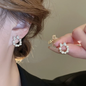 Elegant silver bow earrings with faux pearls and zircons shown on ear and held by hand
