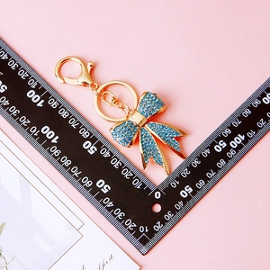 Size measurement of golden metal bow keychain with blue rhinestones on pink background