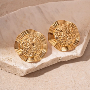 Detail view of gold geometric earrings with hammered metal texture on a stone pedestal