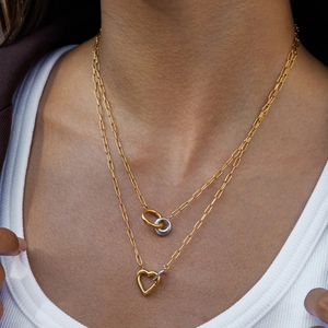 Close-up of dual-layer necklace with gold-silver rings and heart pendant on model