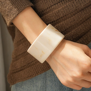 Detail of wide cream resin cuff bracelet with brown marble texture on a model sweater
