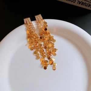 Close-up of long gold tassel earrings with square zircons and dangling metallic sequins