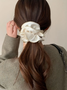 Détail d'un chouchou en satin beige avec bordure dorée sur une coiffure en queue de cheval