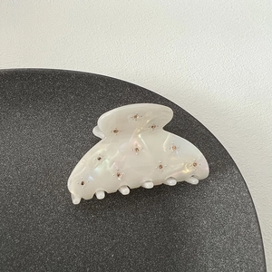 Detail of a pearl white hair claw clip with small pink rhinestones on a textured base