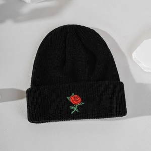 Close-up of a black knitted beanie featuring detailed red rose embroidery on a stone base