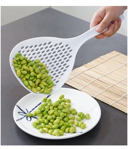 Detailed close-up of a white long-handled slotted spoon draining green soybeans onto a plate