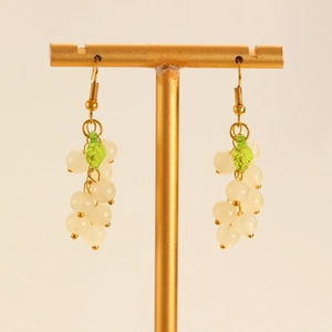 Detail view of grape-shaped drop earrings with white beads and green leaf on gold stand