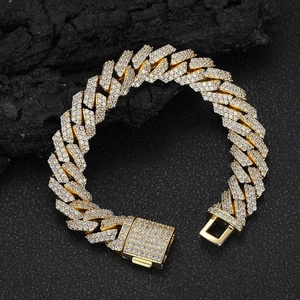 Hip hop gold Cuban link bracelet with diamond pavé settings on a dark textured rock surface