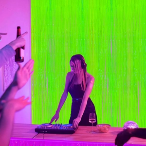 Neon party scene featuring a green tinsel fringe curtain backdrop with DJ table
