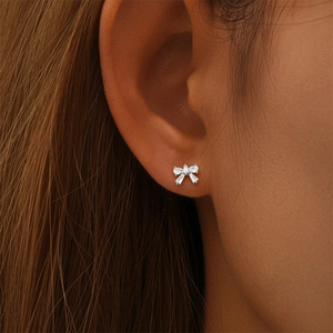 Detail of silver S925 bow stud earring with sparkling cubic zirconia on model's ear
