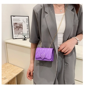 Detail of purple mini crossbody bag with heart buckle and gold chain strap on model