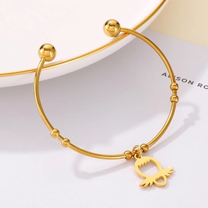 Detailed shot of a gold open cuff bracelet featuring a heart wing charm on a ceramic tray